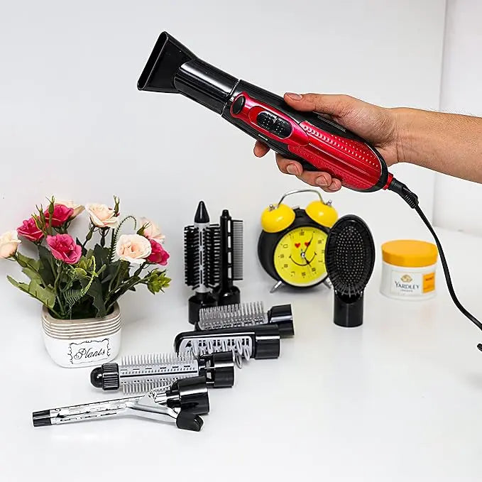 Hand holding a red and black hair dryer with attachments on a white surface.