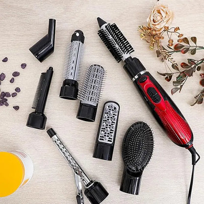 Set of hair styling tools including a red and black hair dryer, brushes, and attachments on a light wooden surface with flowers.